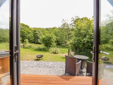 A view through open glass doors to a garden with outdoor chairs and table and a fire pit at Briallen in Bontddu near Dolgellau