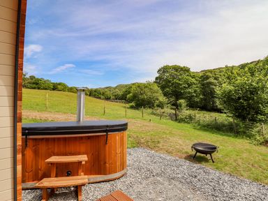 An outdoor area with a wooden hot tub small wooden steps and a fire pit on gravel and grass at Briallen in Bontddu near Dolgellau