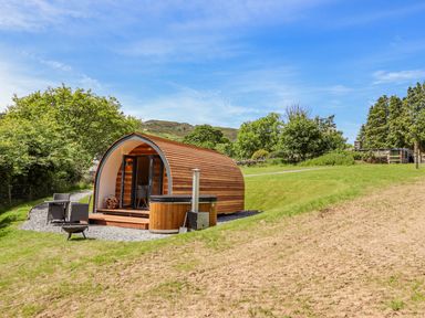 A wooden pod with a hot tub and outdoor seating in a grassy area with trees at Briallen in Bontddu near Dolgellau