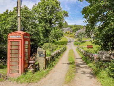 A narrow country road leading to stone houses with a red telephone booth and stone wall at Briallen in Bontddu near Dolgellau