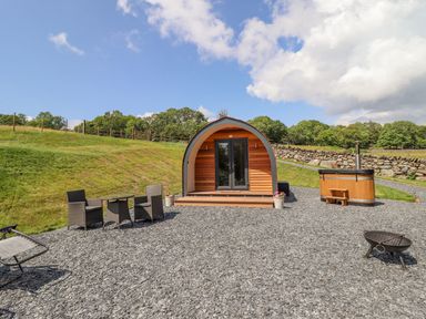 An outdoor area with a wooden pod cabin a hot tub a table with chairs and a fire pit at Eirlys in Bontddu near Dolgellau