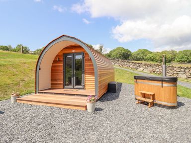 A wooden pod with double glass doors and a small wooden hot tub on gravel outside at Eirlys in Bontddu near Dolgellau