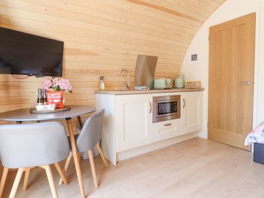 A small kitchen with a dining table two chairs a wall mounted television and wooden door at Eirlys in Bontddu near Dolgellau