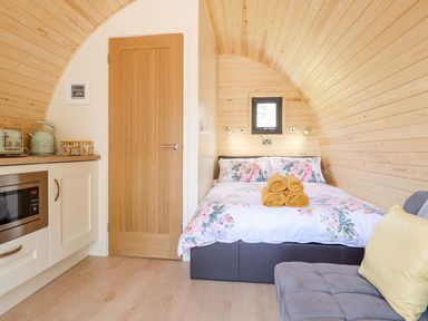 A bedroom with a floral bedspread and rolled towels next to a kitchen area with a microwave and appliances at Eirlys in Bontddu near Dolgellau