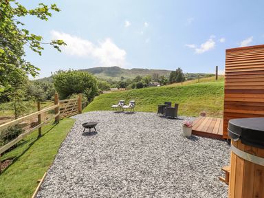 An outdoor area with two lounge chairs a small table with two chairs a fire pit and a wooden building at Eirlys in Bontddu near Dolgellau