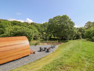 An outdoor area with a wooden pod structure, patio furniture, a gravel ground, and green trees at Eirlys in Bontddu near Dolgellau