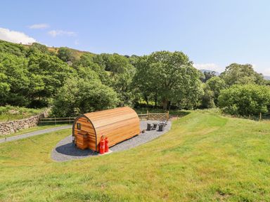 A wooden pod structure on gravel surrounded by grass trees and hills at Eirlys in Bontddu near Dolgellau