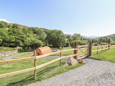 A fenced grassy area with a wooden gate a gravel path and a wooden pod in the countryside at Eirlys in Bontddu near Dolgellau