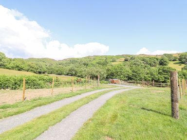 A gravel driveway between wooden and wire fences in a rural landscape with trees and hills at Eirlys in Bontddu near Dolgellau