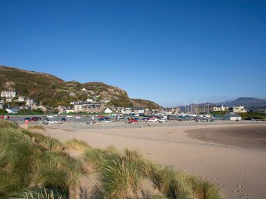 A beach with sand dunes grass parked cars and houses near hills at Eirlys in Bontddu near Dolgellau