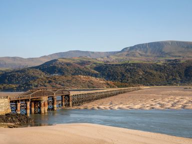 A long iron and stone railway bridge across an estuary with hills in the background at Eirlys in Bontddu near Dolgellau