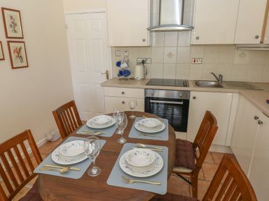 A kitchen with a dining table set for four with plates glasses and cutlery at Kites - 52 Gower Holiday Village in Scurlage near Port Eynon and Rhossili