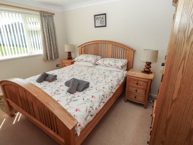 A bedroom with a wooden bed and bedside tables with lamps at Kites - 52 Gower Holiday Village in Scurlage near Port Eynon and Rhossili