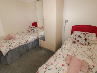 A bedroom with two single beds with floral bedding a wardrobe and a floor lamp at Kites - 52 Gower Holiday Village in Scurlage near Port Eynon and Rhossili
