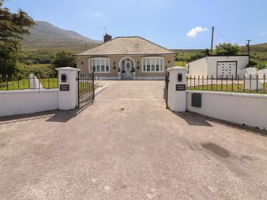 A bungalow house with a driveway and gated entrance set against a mountain backdrop at Killelton Cottage in Camp County Kerry