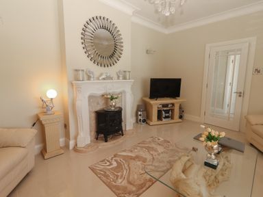 A living room with a glass coffee table with flowers on it a decorative fireplace a television on a stand and beige sofas at Killelton Cottage in Camp County Kerry
