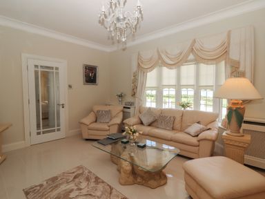 A living room with beige leather sofas a glass coffee table a chandelier and large windows at Killelton Cottage in Camp County Kerry