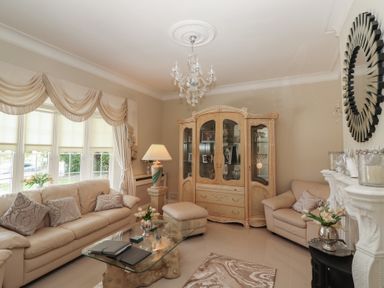 A living room with beige sofas a glass coffee table a decorative cabinet and a chandelier at Killelton Cottage Camp County Kerry