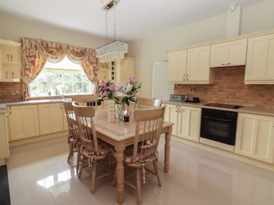 A kitchen with wooden dining table and chairs flowers on table and cream cabinets at Killelton Cottage Camp County Kerry