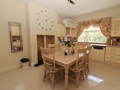 A kitchen with a dining table and chairs a wall clock and a window with curtains at Killelton Cottage Camp County Kerry