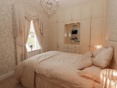 A bedroom with a bed and built-in wardrobes with a mirror and flowers near a window at Killelton Cottage in Camp County Kerry