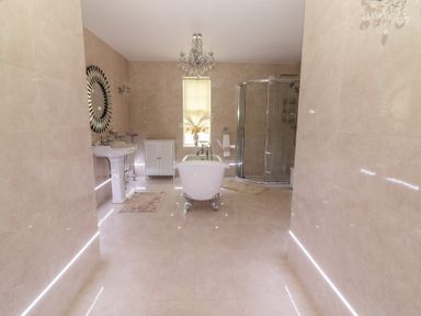 A bathroom with a freestanding bathtub in the center a round mirror above a sink a glass shower enclosure and a window at Killelton Cottage in Camp County Kerry