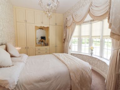 A bedroom with a bed next to a bay window with curtains and built-in wardrobes with a mirror at Killelton Cottage in Camp County Kerry