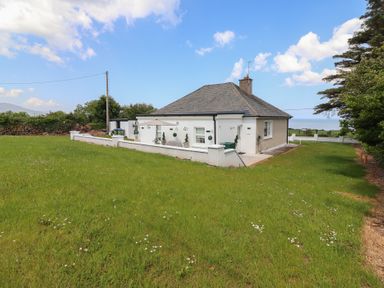 A white house with a slate roof surrounded by grass and trees at Killelton Cottage in Camp County Kerry