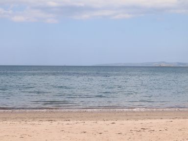 A sandy beach with calm sea water and a distant coastline under a partly cloudy sky at Killelton Cottage in Camp County Kerry