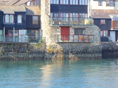 Stone and wood waterfront buildings with balconies over a stone seawall and water at Tobys Quay in Falmouth