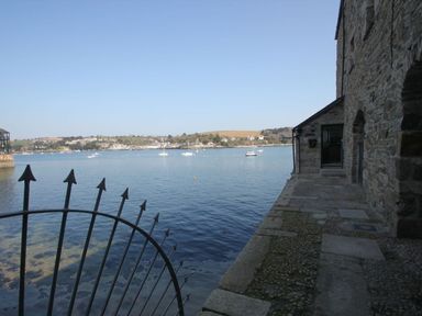 A stone building beside a body of water with boats and a metal fence at Tobys Quay in Falmouth