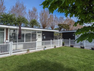 A grassy yard with potted plants and white railing outside single-story buildings at 99 Cherry Park in Chapel St Leonards