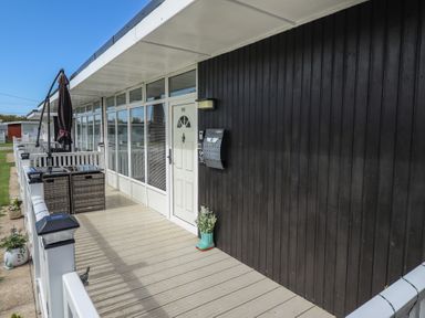 A porch with a white door black wall and outdoor furniture at 99 Cherry Park in Chapel St Leonards