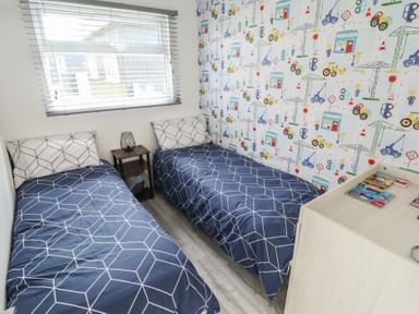 A bedroom with two single beds and a nightstand under a window at 99 Cherry Park in Chapel St Leonards