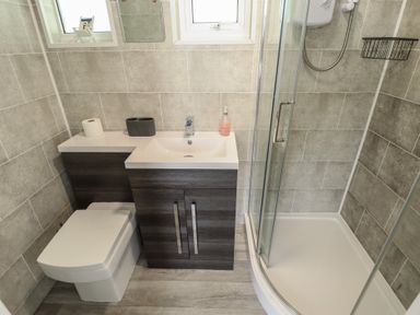 A bathroom with a toilet, a sink with a cabinet, and a shower cubicle at 99 Cherry Park in Chapel St Leonards