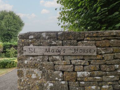 A stone wall with a wooden sign displaying the name St. Mary's House at St. Marys House Church Westcote near Bledington
