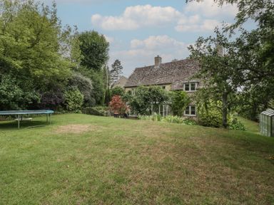A garden with a house, trampoline, and greenhouse at St. Marys House Church Westcote near Bledington