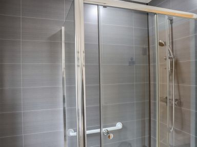 A shower with glass doors and showerhead at Bungalow 15 Eamont Park Penrith