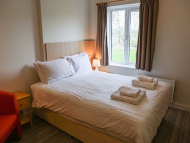 A bedroom with a bed, nightstand, and window at Bedroom 7 in Penrith