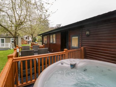 A wooden deck with a hot tub and outdoor dining set next to a cabin at Robins Lodge White Cross Bay near Troutbeck Bridge