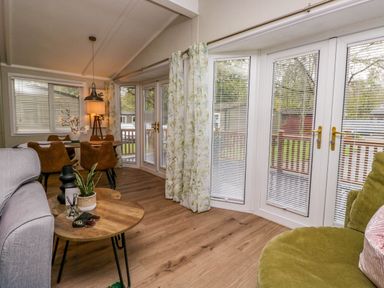 A living room with a wooden table and chairs a gray sofa and a green chair with floral curtains at Robins Lodge White Cross Bay near Troutbeck Bridge
