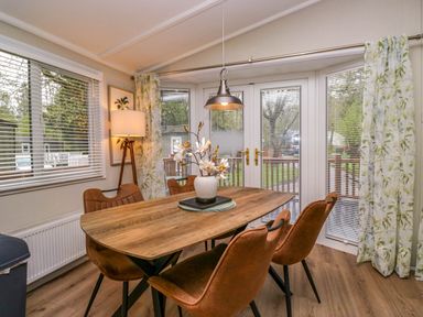 A dining room with a wooden table and brown chairs near windows and glass doors at Robins Lodge White Cross Bay near Troutbeck Bridge