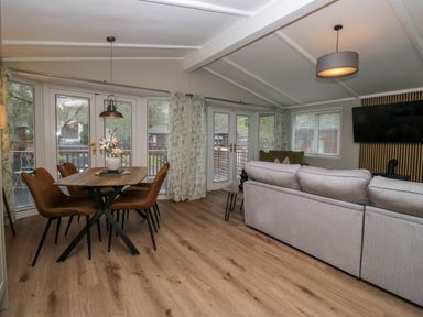 A living room with a dining table and chairs a sofa and a wall-mounted television at Robins Lodge in White Cross Bay near Troutbeck Bridge