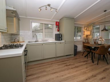 A kitchen and dining area with cabinets a gas stove a round table with chairs and windows with blinds at Robins Lodge in White Cross Bay near Troutbeck Bridge
