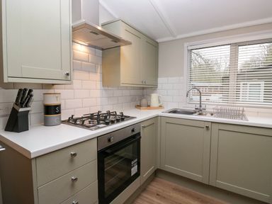 A kitchen with cabinets a gas stove an oven a sink and a window with blinds at Robins Lodge in White Cross Bay near Troutbeck Bridge