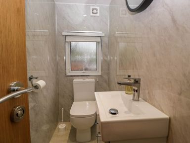 A small bathroom with a toilet a sink a window and a toilet brush at Robins Lodge White Cross Bay near Troutbeck Bridge