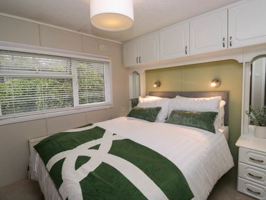 A bedroom with a bed with green and white bedding next to a window and white overhead cabinets at Robins Lodge in White Cross Bay near Troutbeck Bridge
