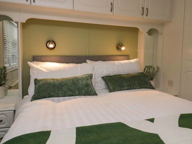 A bed with white bedding and green pillows under built in white cabinets with wall lights at Robins Lodge in White Cross Bay near Troutbeck Bridge