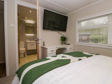 A bedroom with a bed green and white blanket desk and wall mounted tv at Robins Lodge White Cross Bay near Troutbeck Bridge