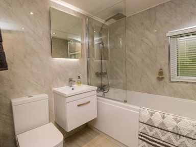 A bathroom with a toilet sink with cabinet bathtub with shower and window blinds at Robins Lodge White Cross Bay near Troutbeck Bridge